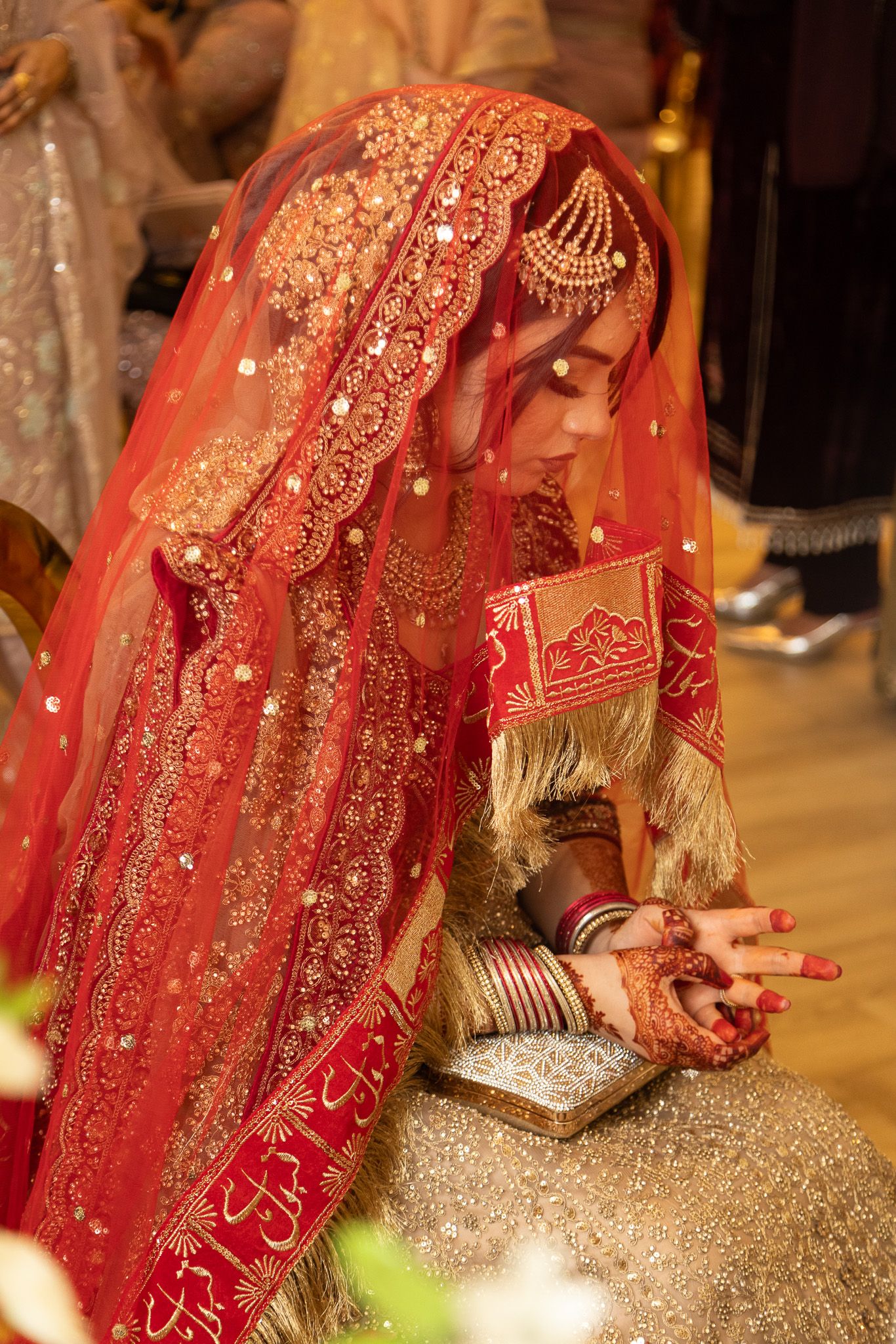 Pakistani bride in red embroidered bridal outfit reading Quran during traditional Nikah ceremony.