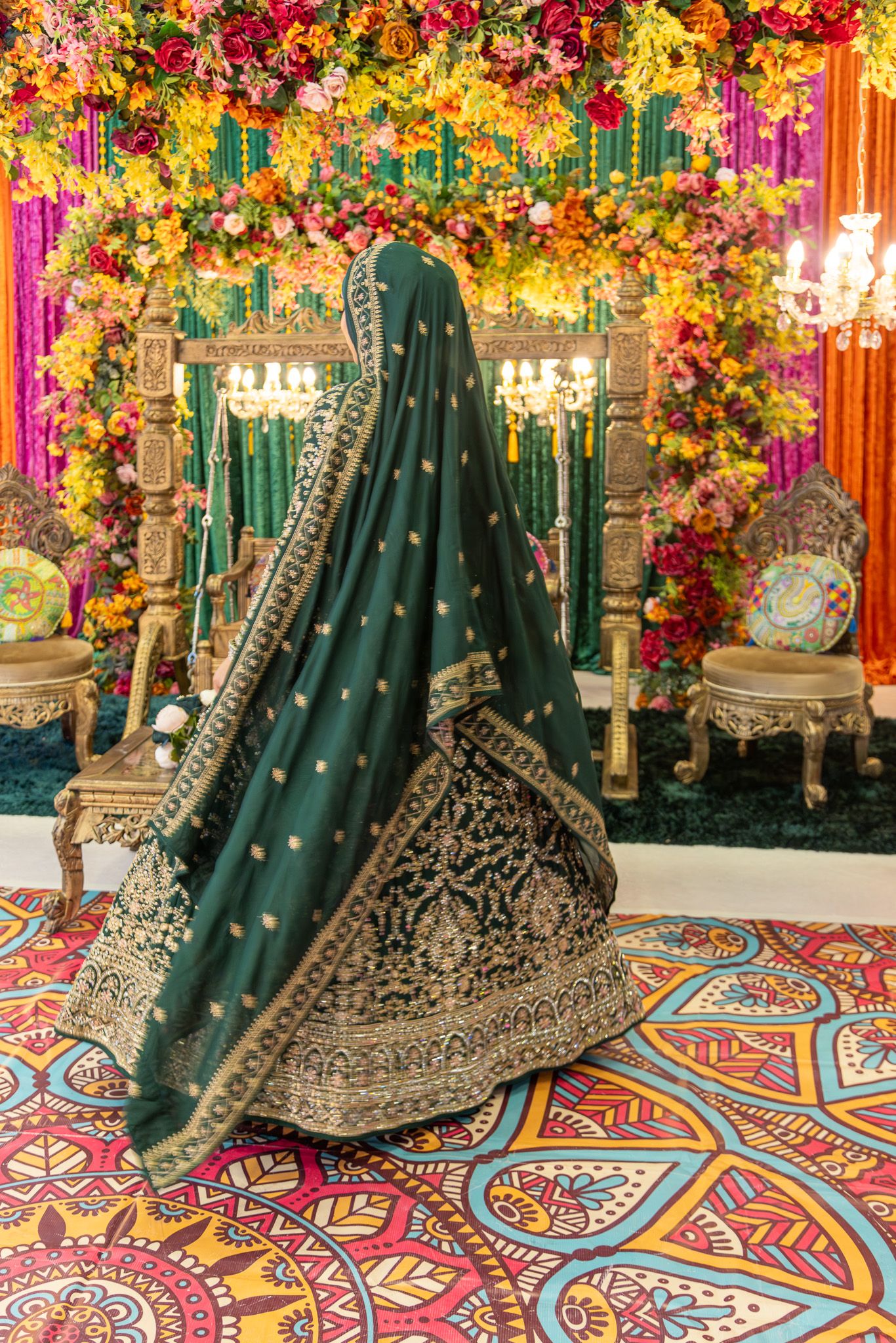 Bride in green embroidered lehenga with dupatta, standing before ornate floral mandap at South Asian wedding in london