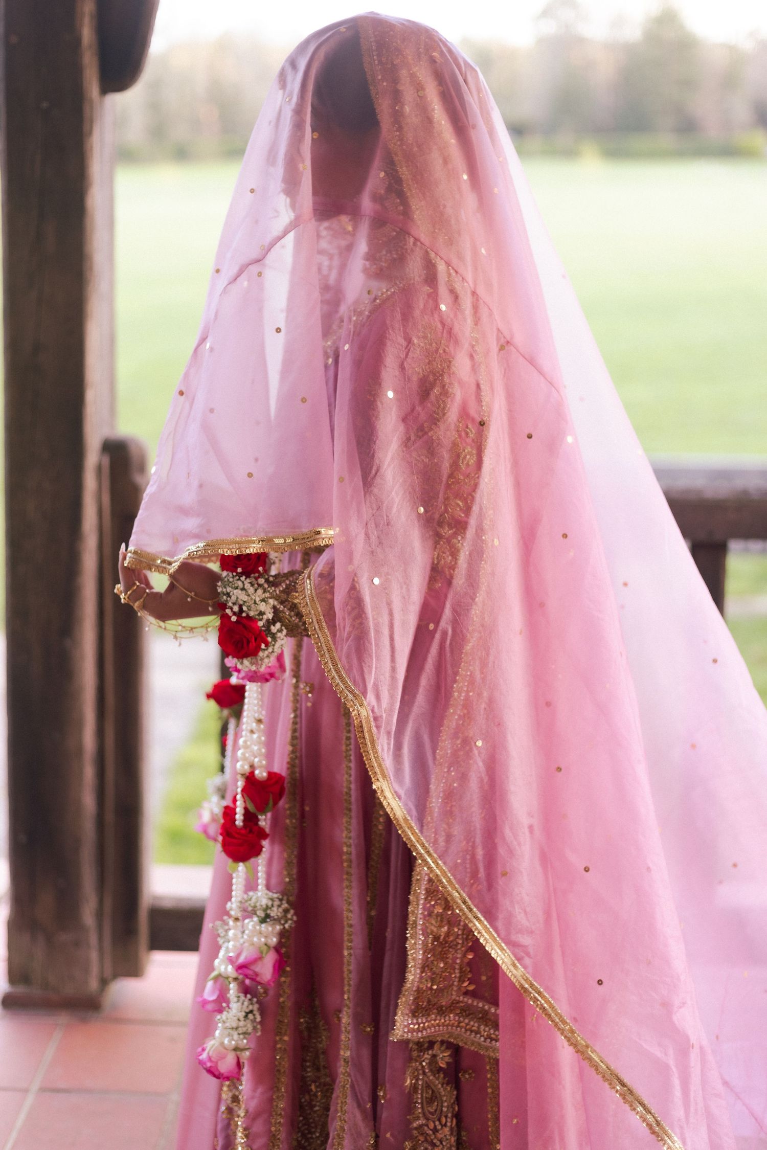 Pink Pakistani  bridal lehenga with gold embroidery and floral garland, bride covered in pink veil in london.