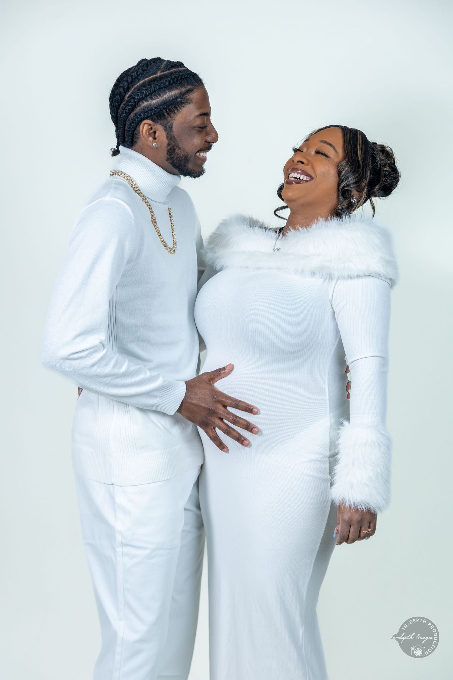 Couple in matching white outfits sharing a tender moment during a maternity photo shoot.