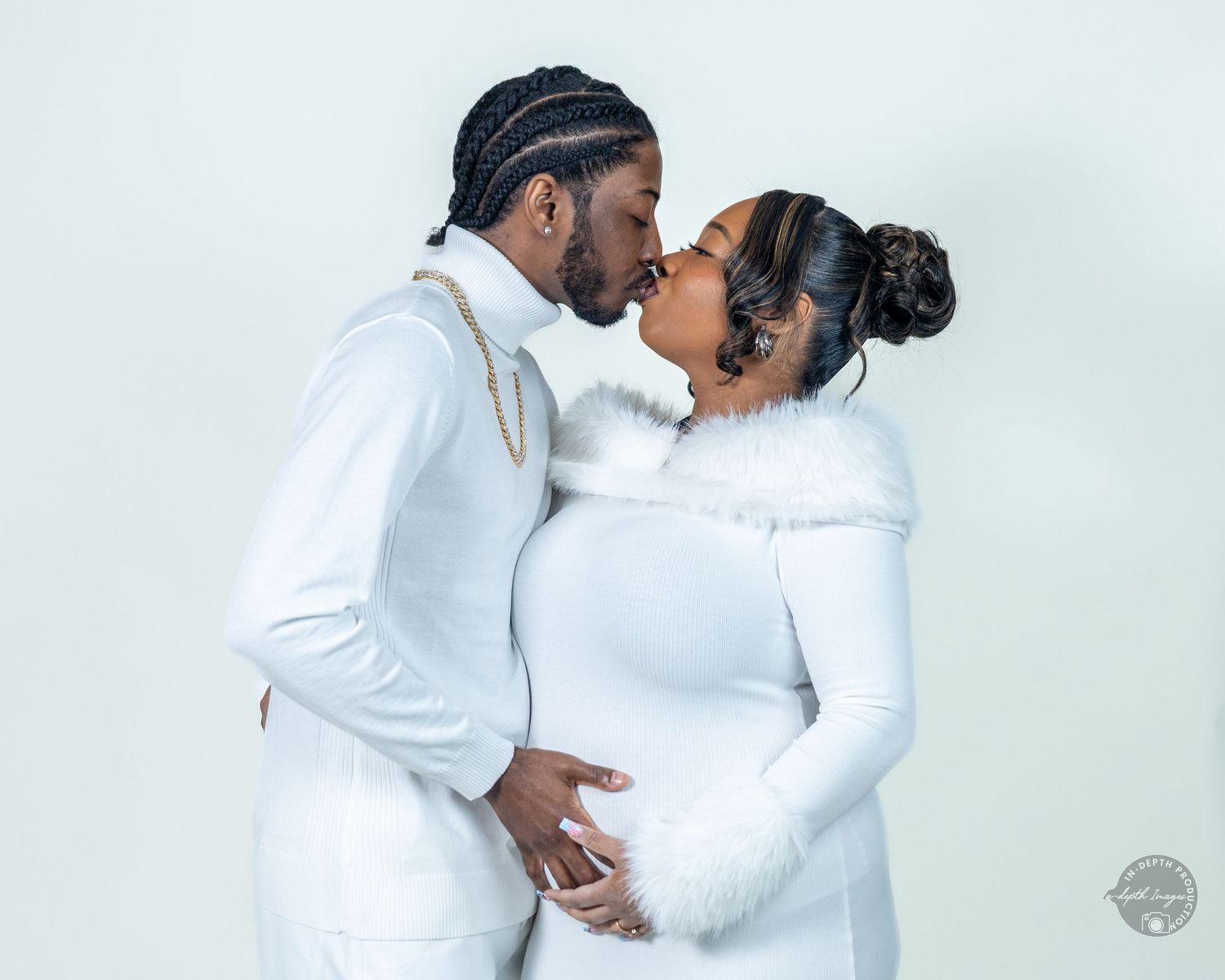 Couple in matching white outfits sharing a kiss during a romantic maternity photo session.