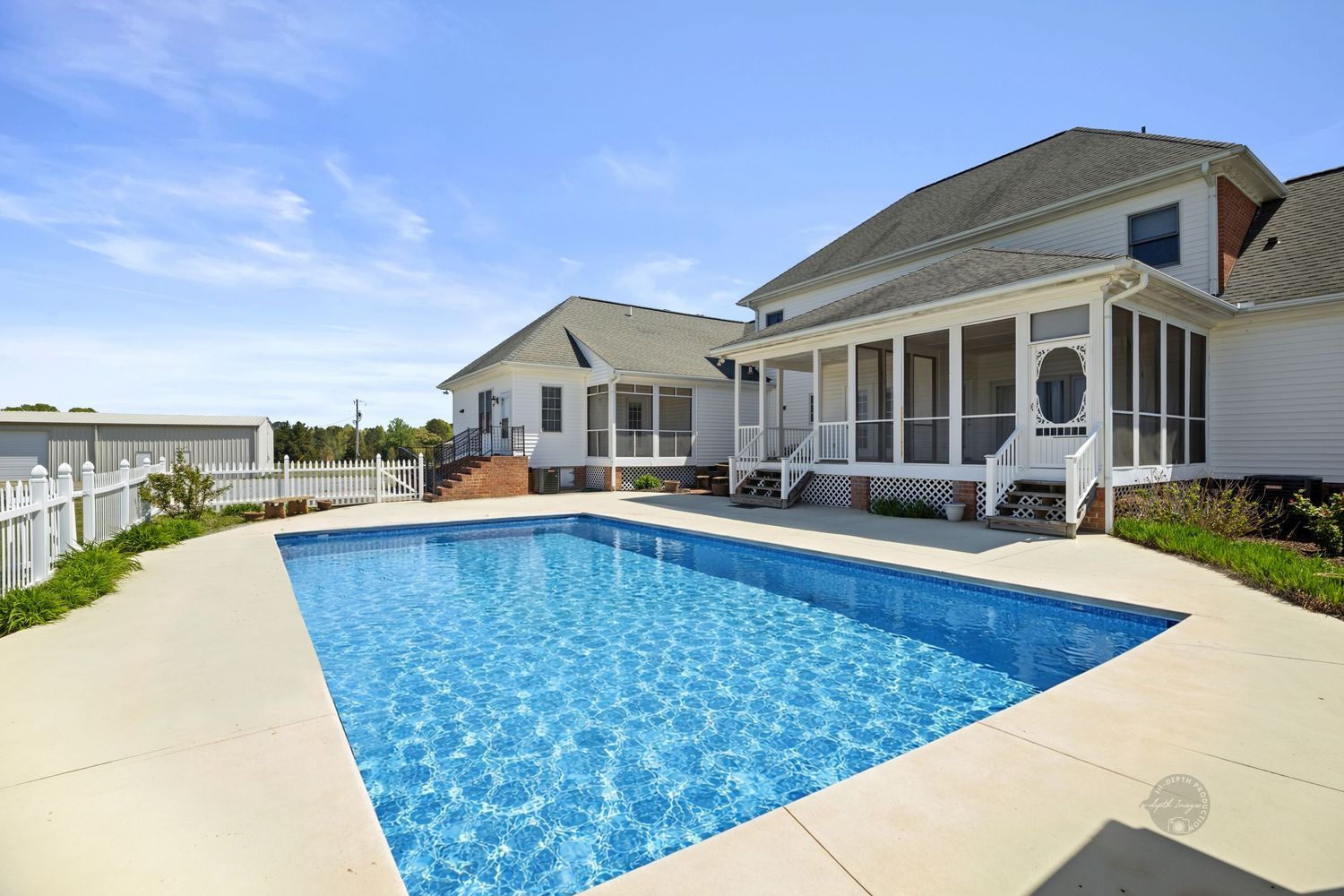 Spacious outdoor pool with clear blue water beside a white house featuring a screened porch on a sunny day.
