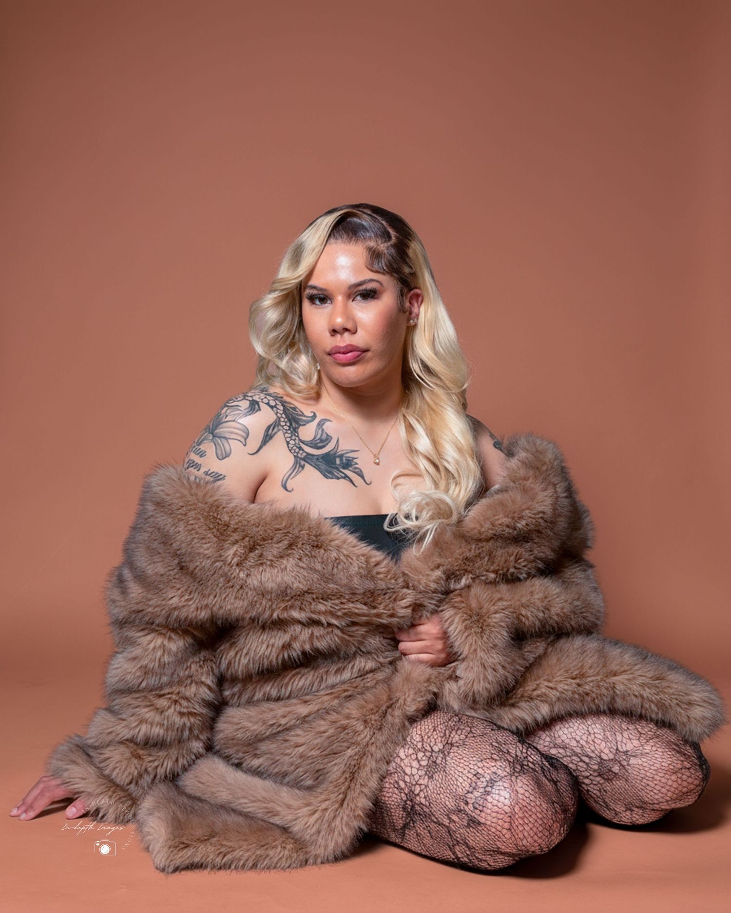 Woman in fur coat with tattoos posing for studio portrait on brown background.