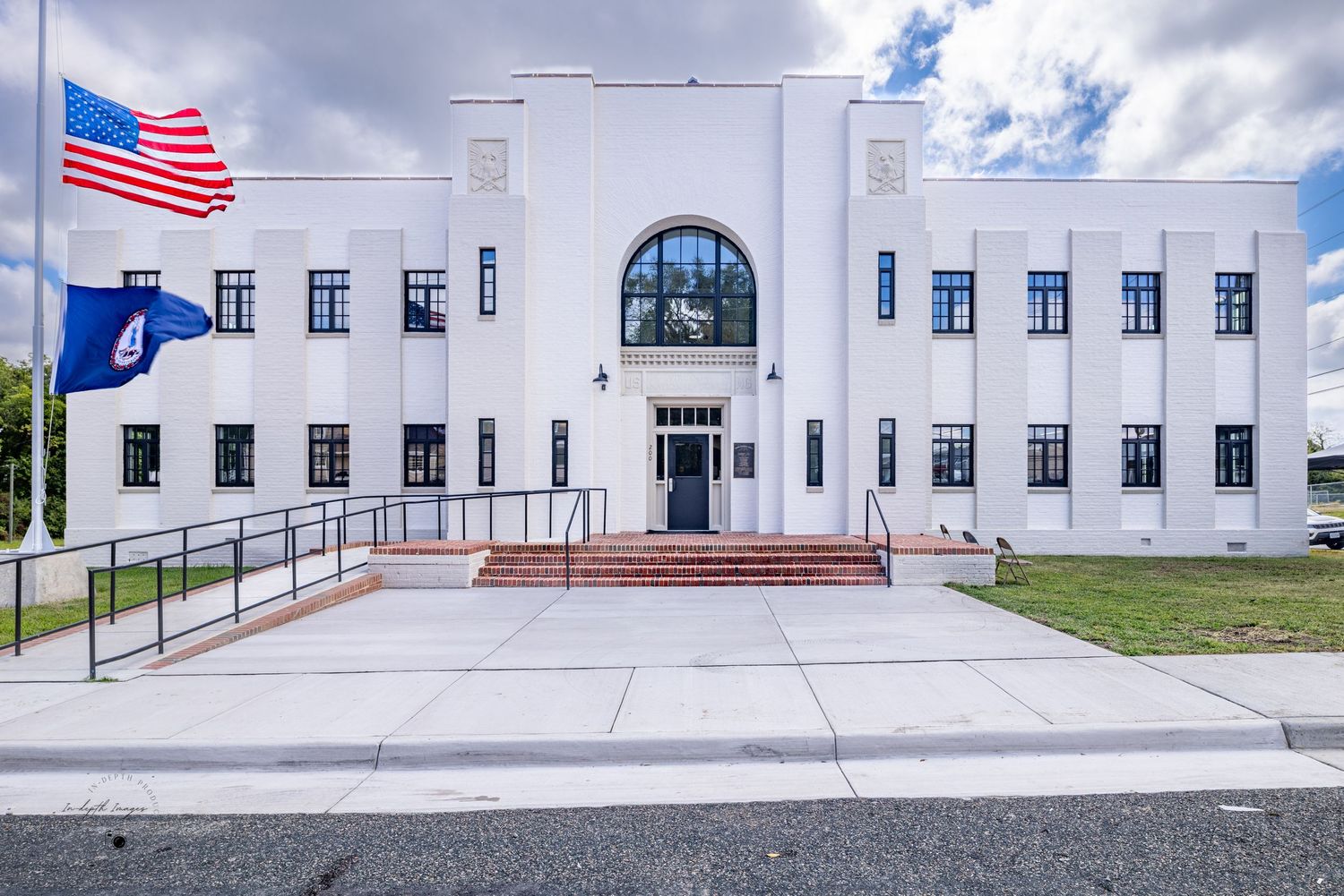 Art Deco white government building with symmetrical facade, arched window, red steps, and American flag displayed.