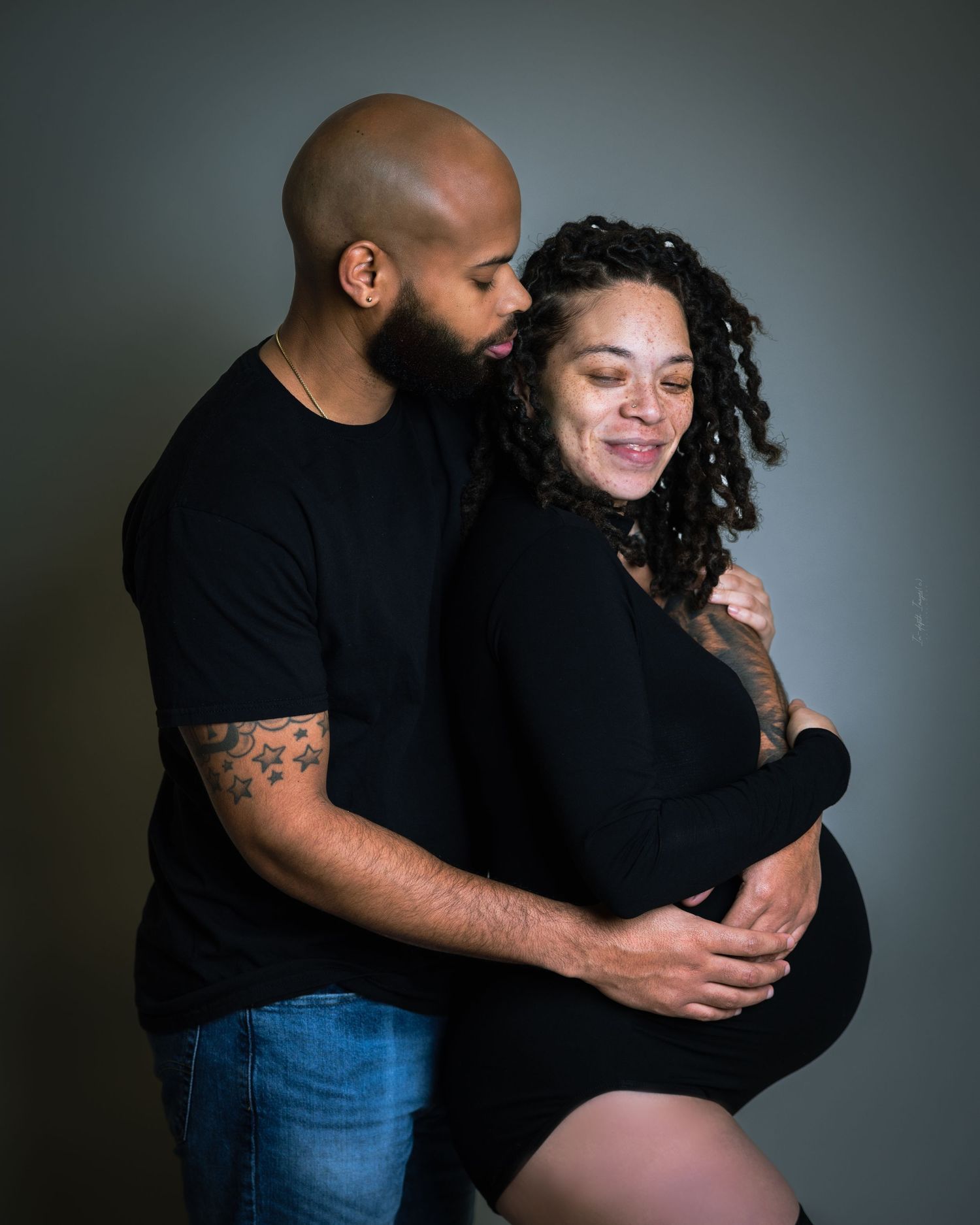 Smiling couple in black outfits sharing a warm embrace during maternity photo session.