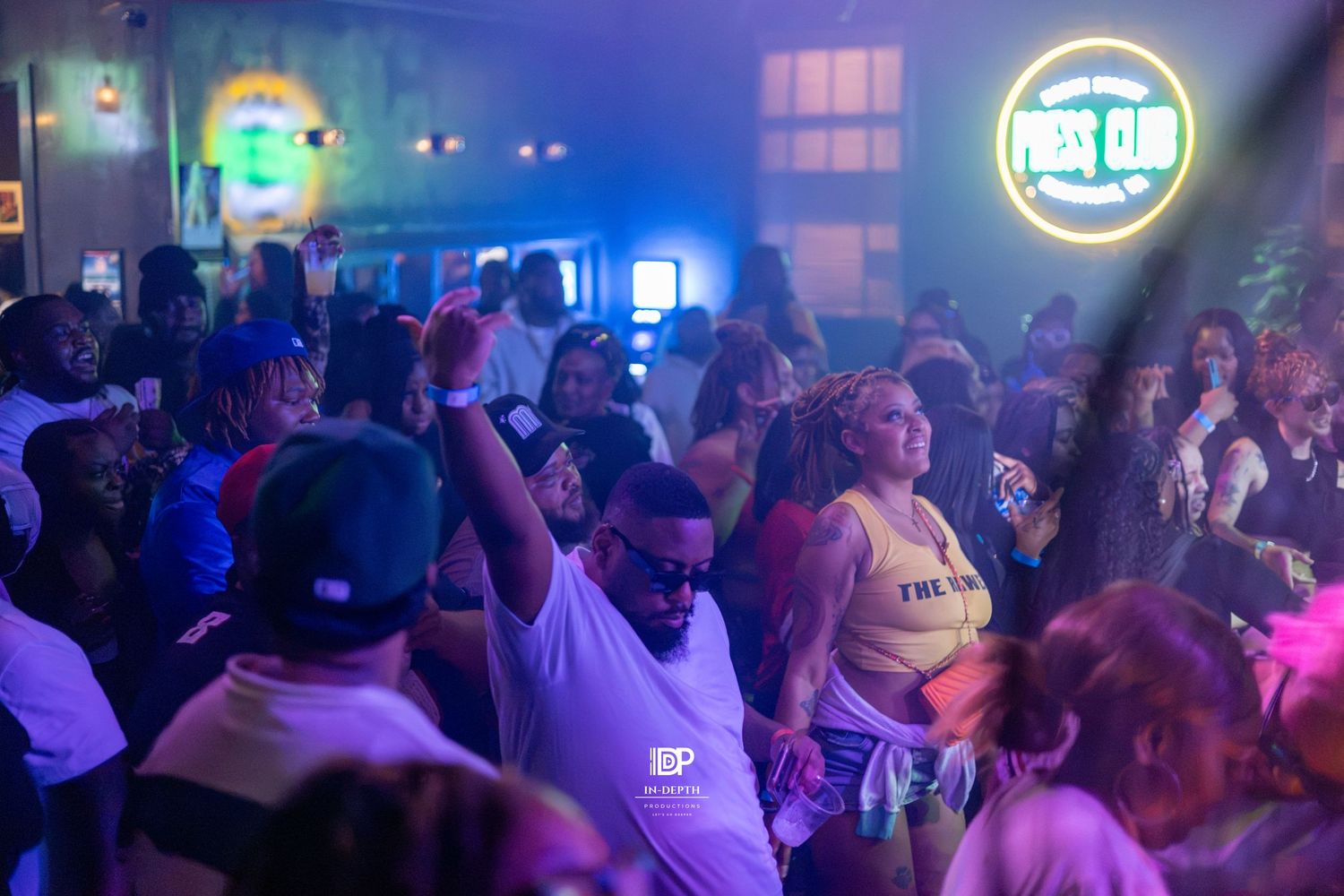 Energetic nightclub crowd dancing under neon lights at Press Club venue with purple and blue lighting.