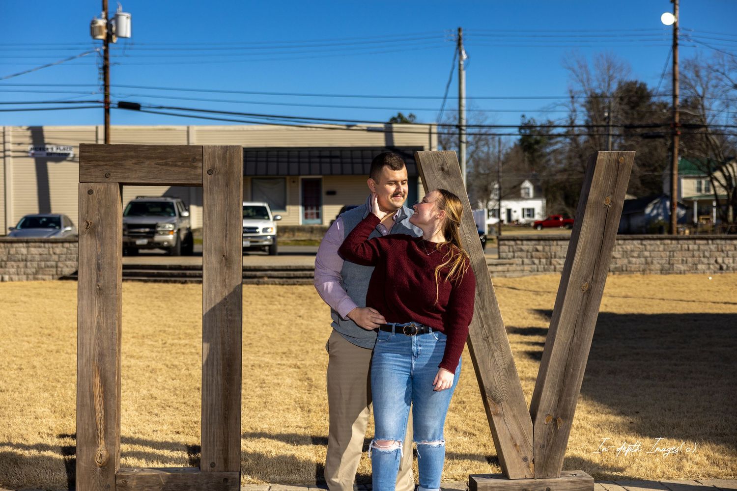Couple shares a romantic moment outdoors near rustic wooden structures on a sunny day.