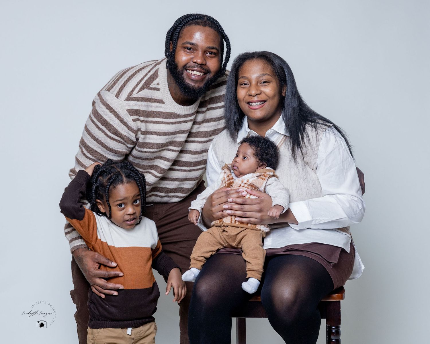 Smiling Black family of four posing together in a professional studio portrait with neutral background.