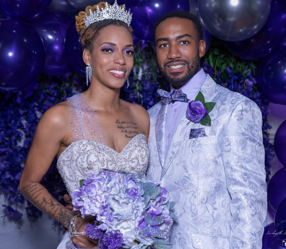 Bride and groom posing at purple-themed wedding, bride wearing crown and gown, groom in floral suit.