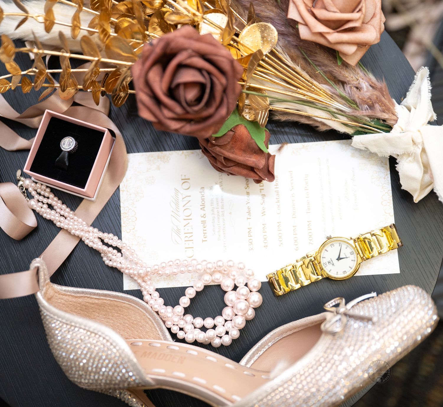 Elegant wedding flat lay with pearl heels, gold watch, diamond ring, pearl necklace, roses, and ornate invitation on dark background.