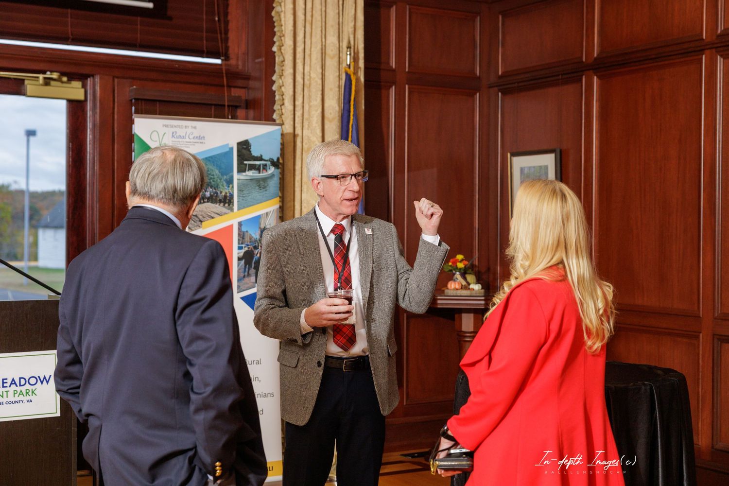 Three professionals engaged in conversation at a networking event in a wood-paneled conference room.