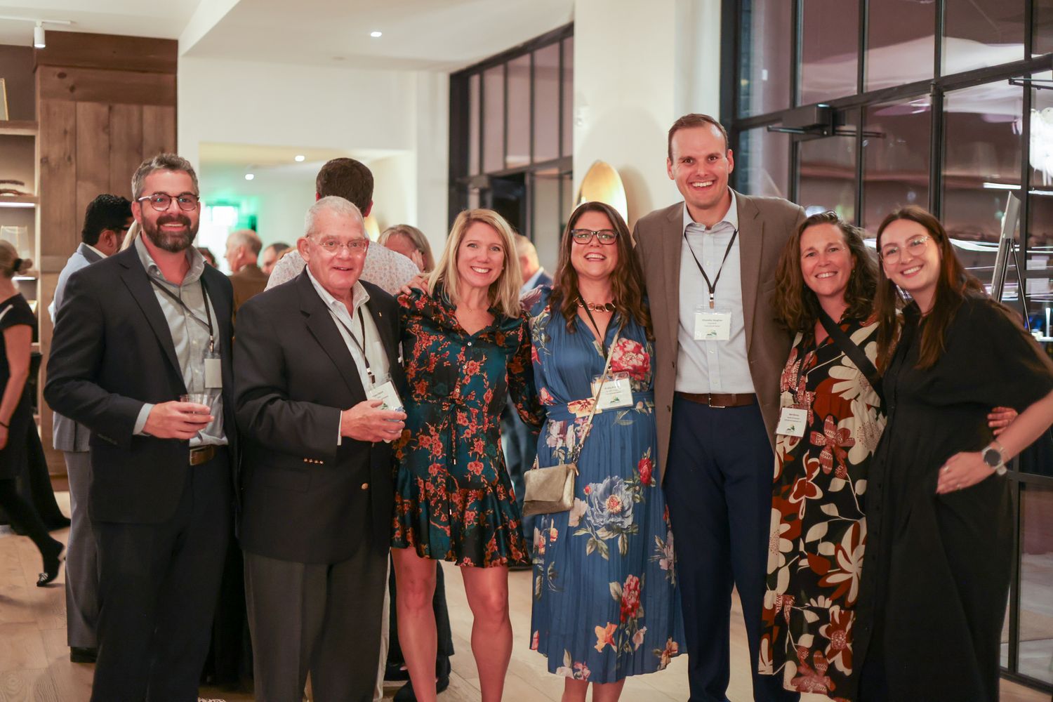 Group of seven professionals smiling together at a corporate networking event in a modern venue.