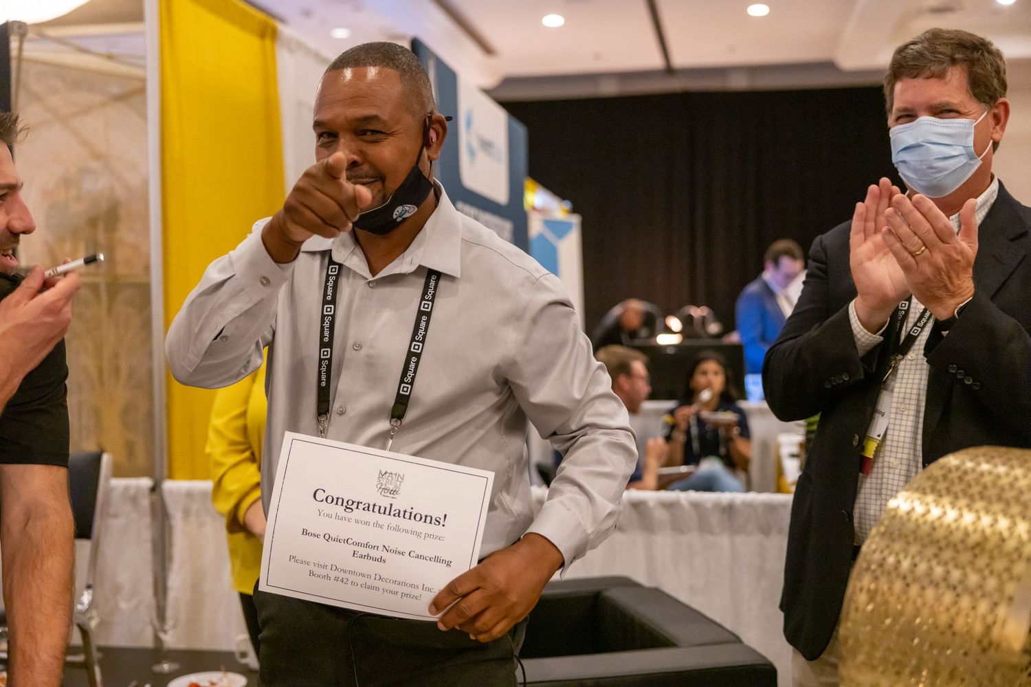 Man proudly holding congratulations certificate at awards ceremony while audience applauds in background.