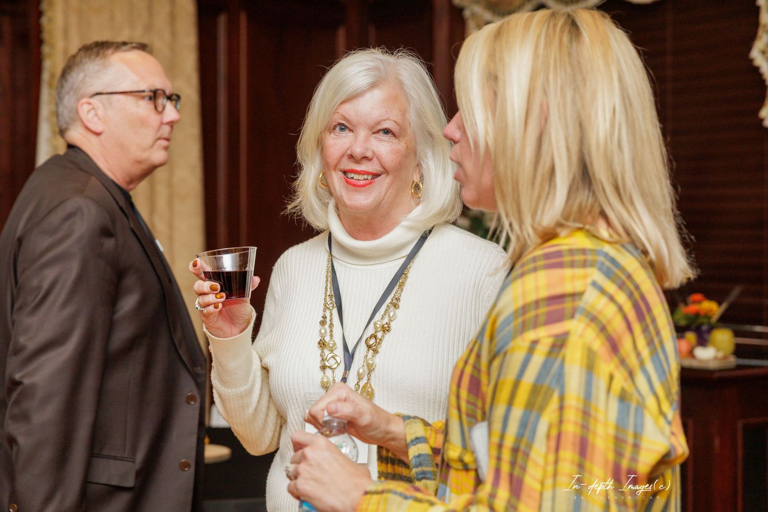 Three elegantly dressed adults socializing at a formal gathering, woman in white holding a wine glass.