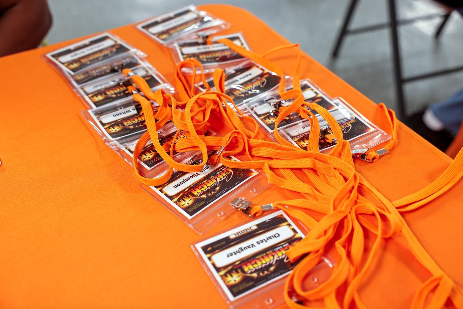 Orange lanyards and printed name badges in clear holders are neatly arranged on an orange tablecloth at a church event check-in table.
