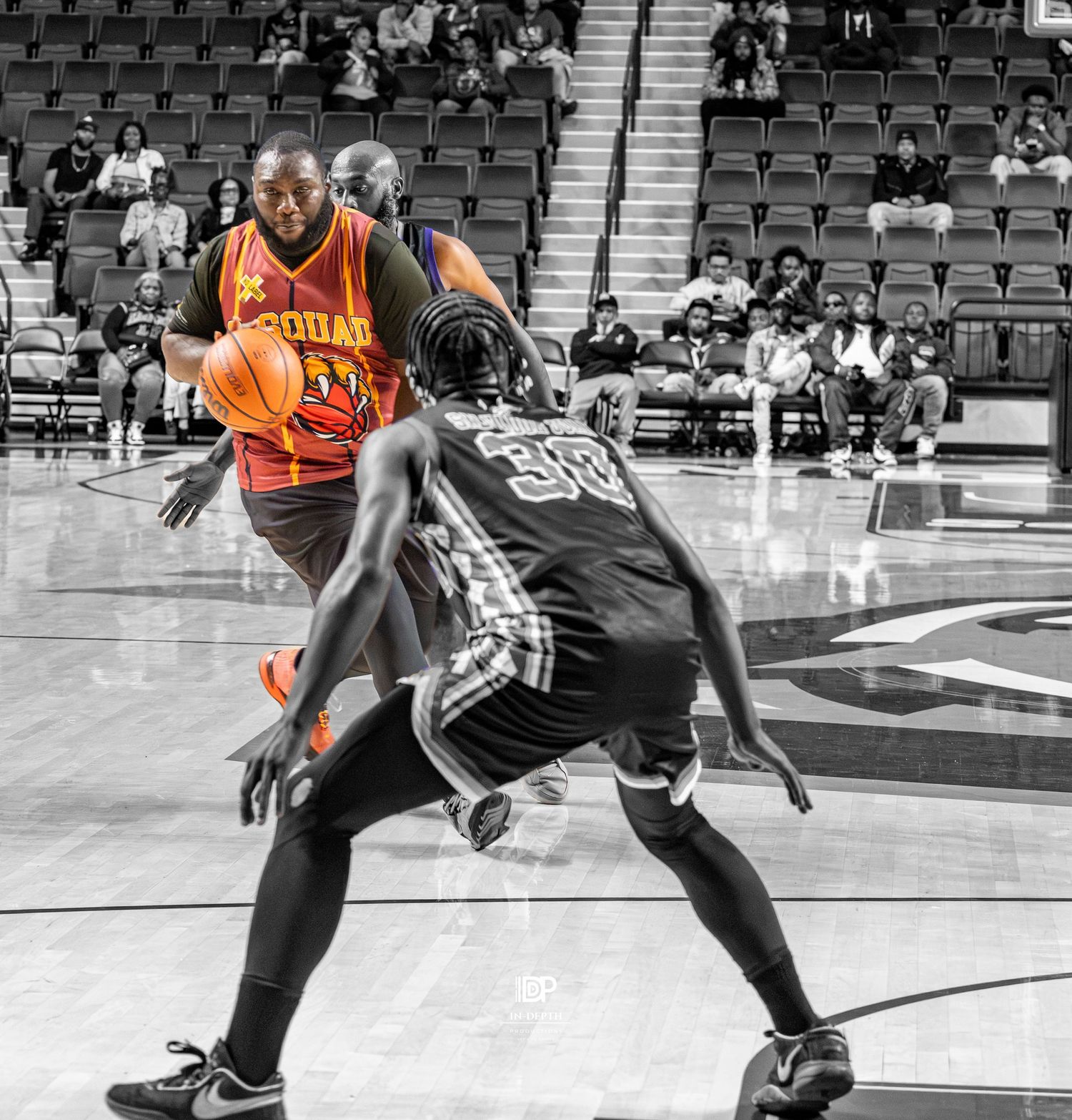 Basketball player in orange jersey dribbles past defender in black uniform during indoor game with selective color effect.