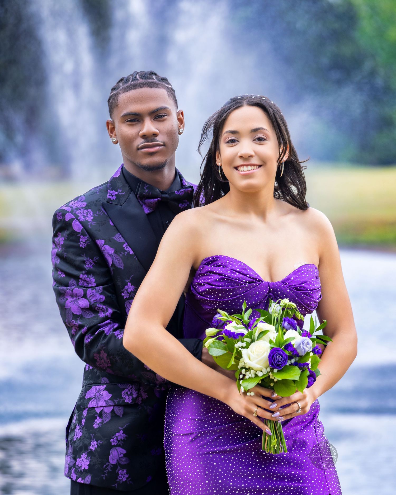 Couple in matching purple outfits posing in front of fountain for prom photos.