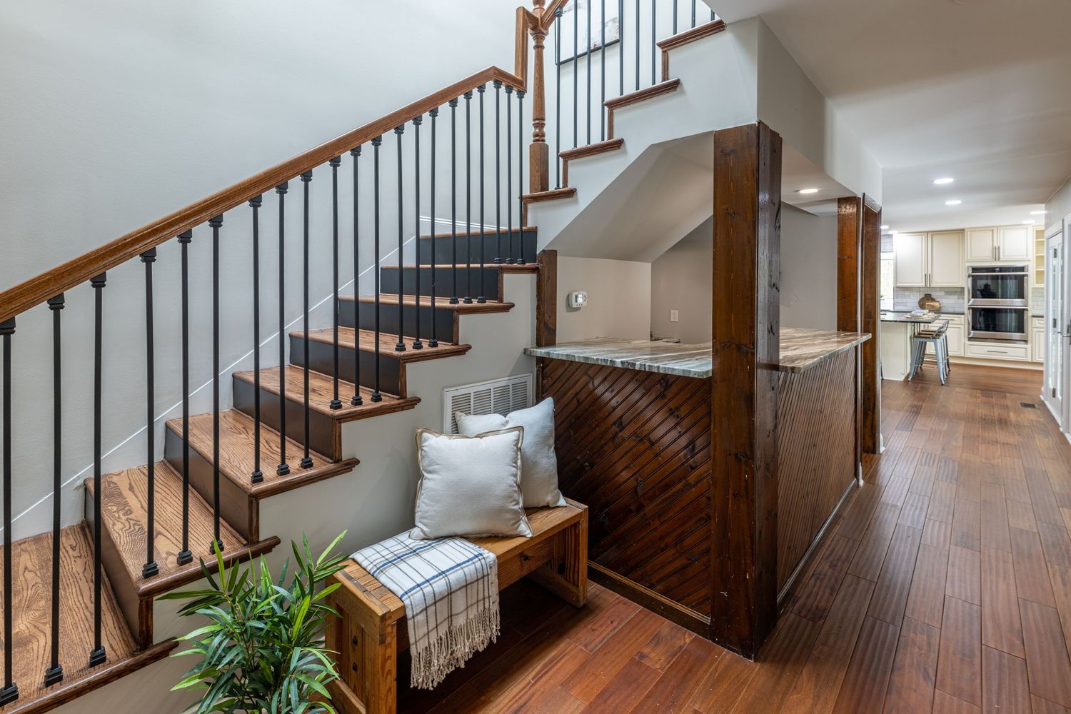 Elegant staircase with wood and black metal balusters leading to an open kitchen in a modern townhome.