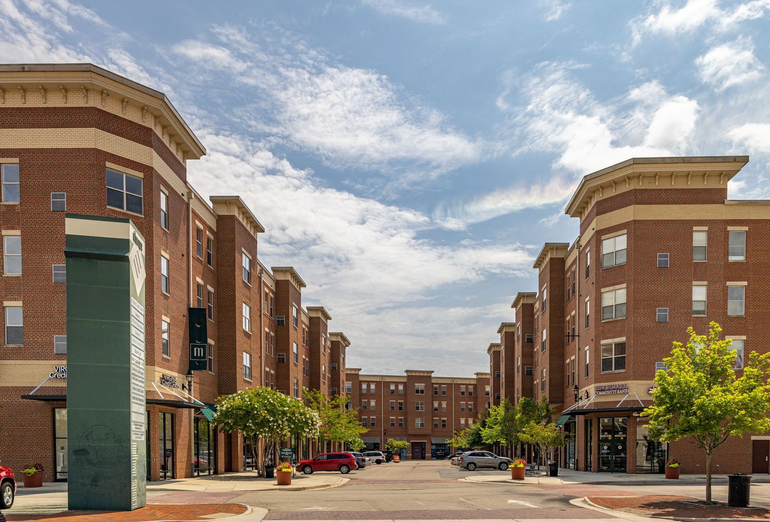 Modern brick mixed-use apartment buildings lining a pedestrian-friendly urban streetscape under a partly cloudy sky.