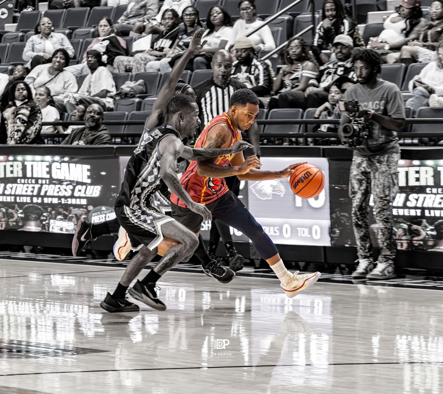 Basketball player in red uniform drives past defender during an indoor game with fans watching in the background.