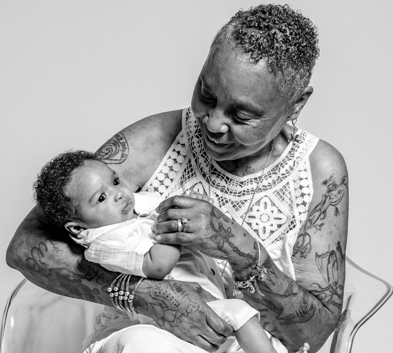 Tattooed person tenderly holding a newborn baby in a black and white portrait photo.