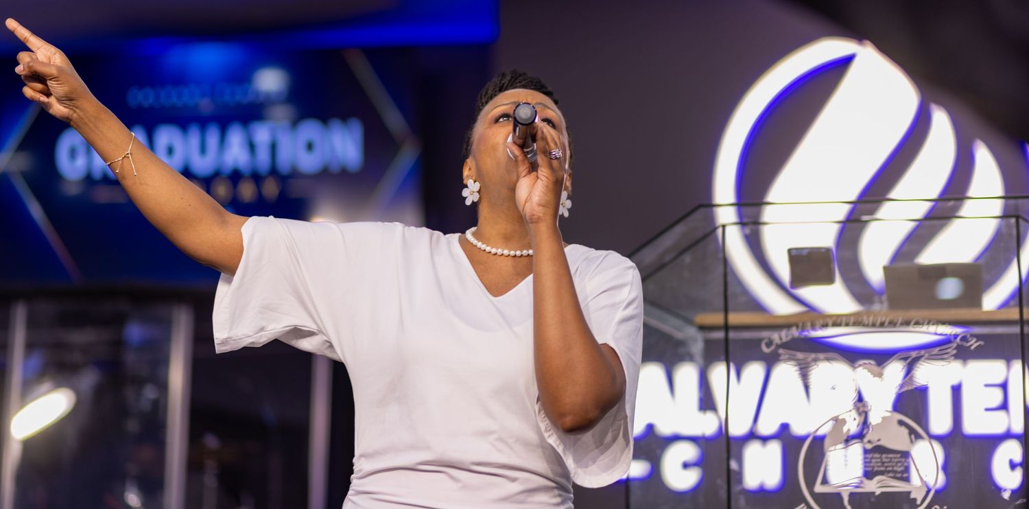 Singer performing passionately on stage at Calvary Temple Church graduation ceremony, pointing upward with microphone.