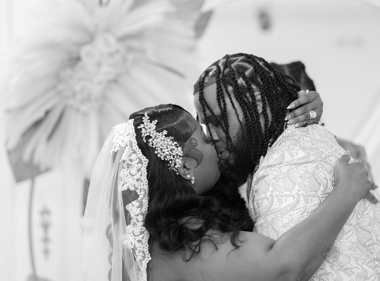 Two brides share a tender kiss during their wedding ceremony in a black and white photo.
