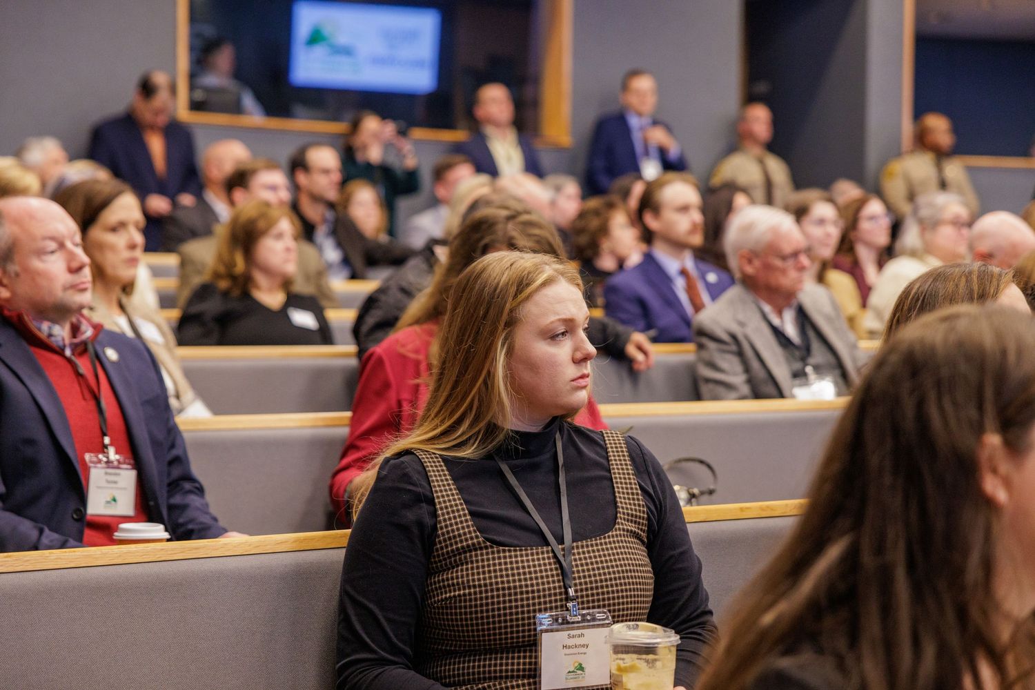 Attendees seated in rows at a professional conference or public meeting, listening attentively in a modern auditorium.