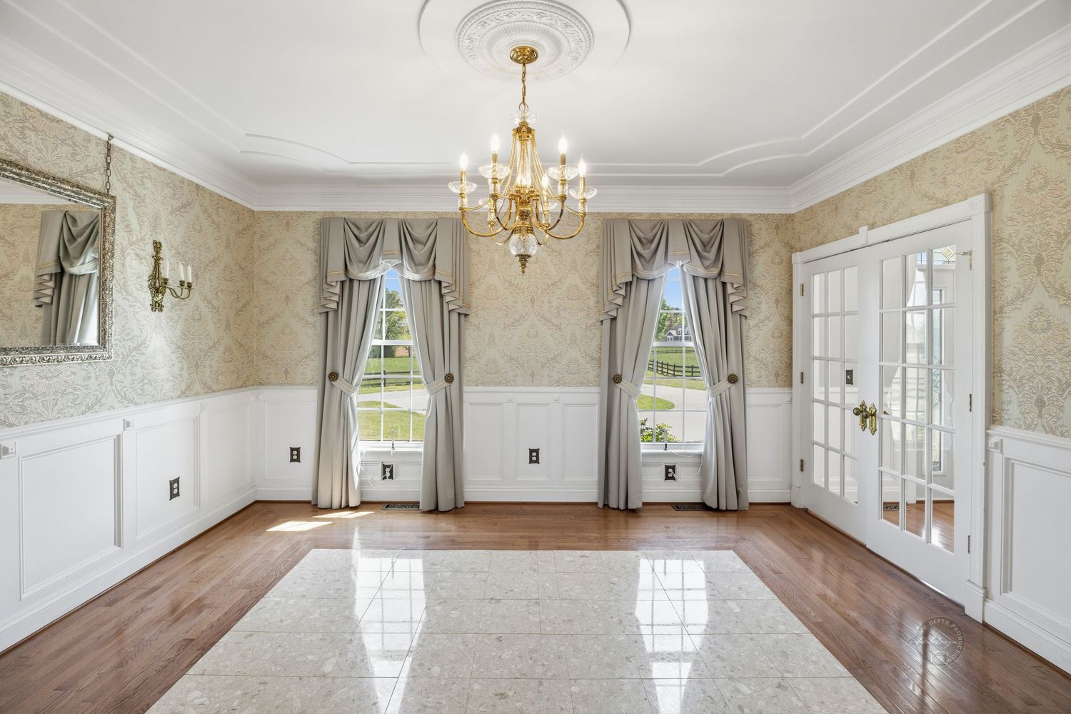 Elegant formal dining room with gold damask wallpaper, wainscoting, chandelier, French doors, and marble tile flooring.