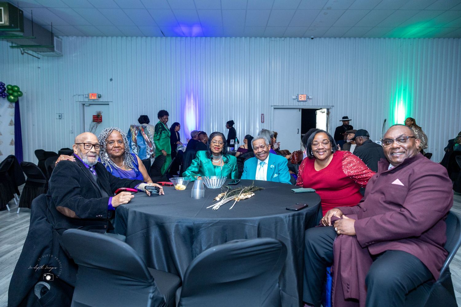 A group of six people smile and pose together at a formal evening banquet event with blue lighting.