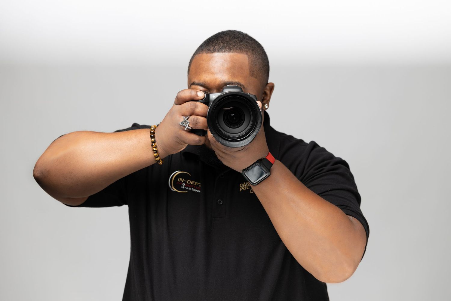 Professional photographer wearing black shirt aiming DSLR camera forward against gray backdrop.