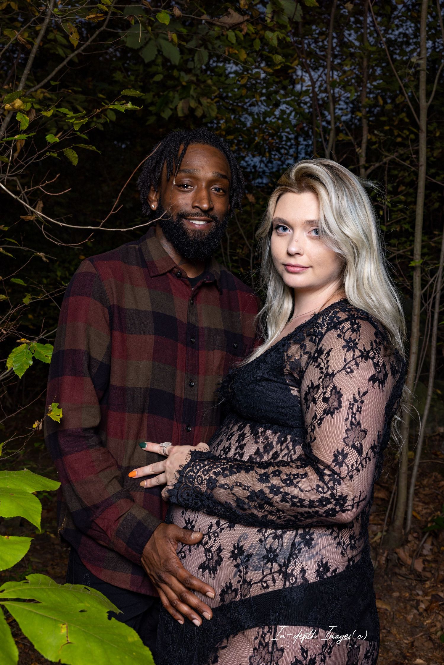 Interracial couple posing together outdoors at night during maternity photo shoot.