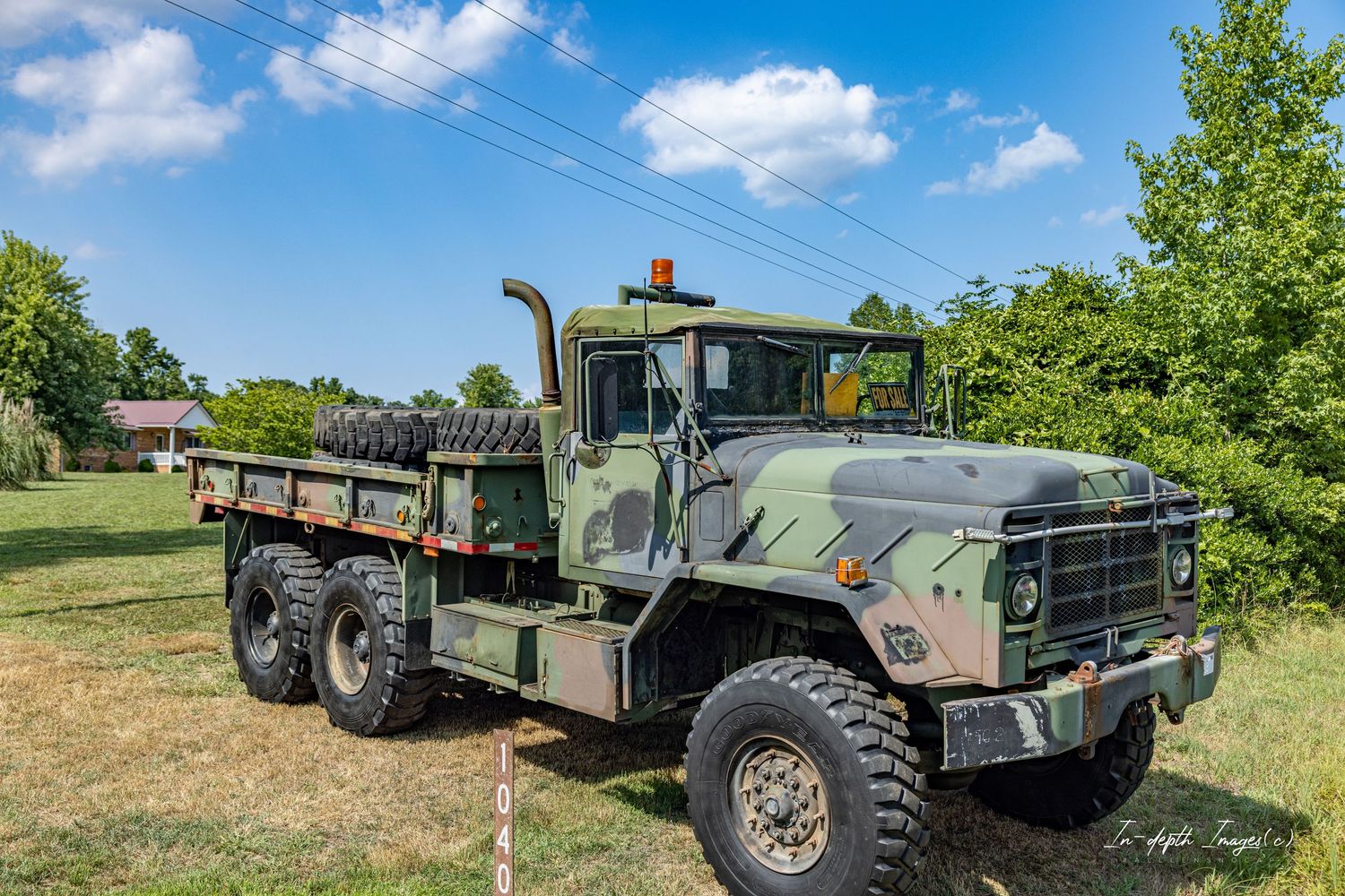 Vintage military olive green 6-wheel cargo truck parked on grass under a bright blue sky with clouds.