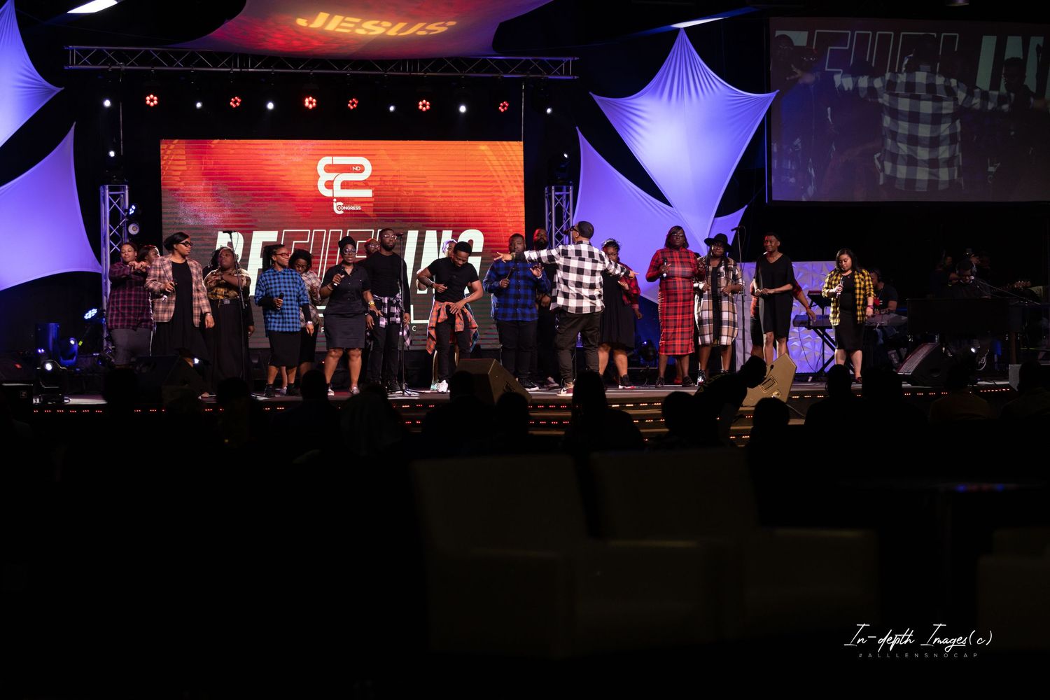 Large group on stage at church event with Jesus banner backdrop.