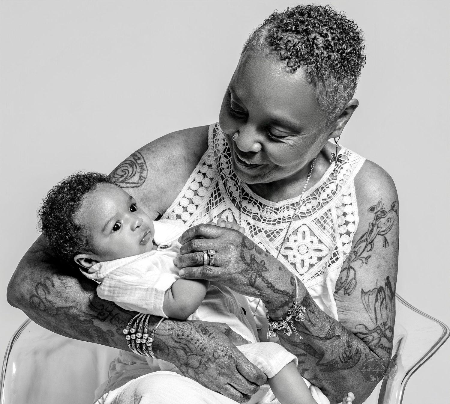 Black and white photo of a heavily tattooed person tenderly cradling a newborn baby, smiling warmly.
