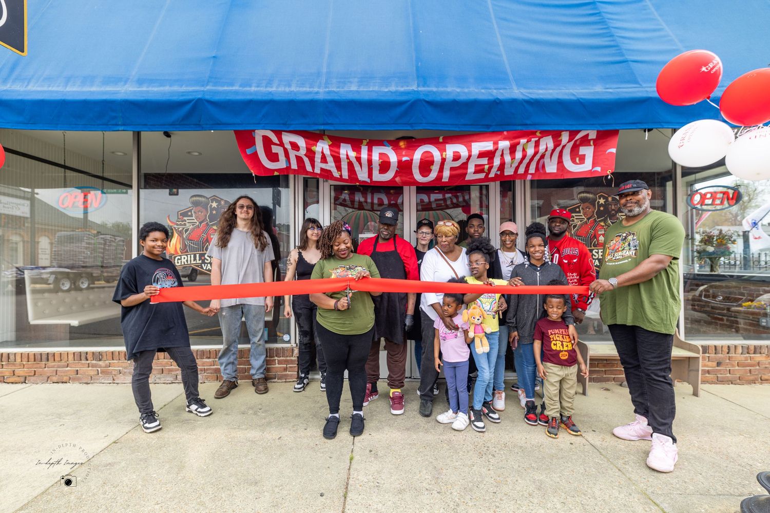 A group of people celebrate a grand opening by cutting a red ribbon outside a storefront.