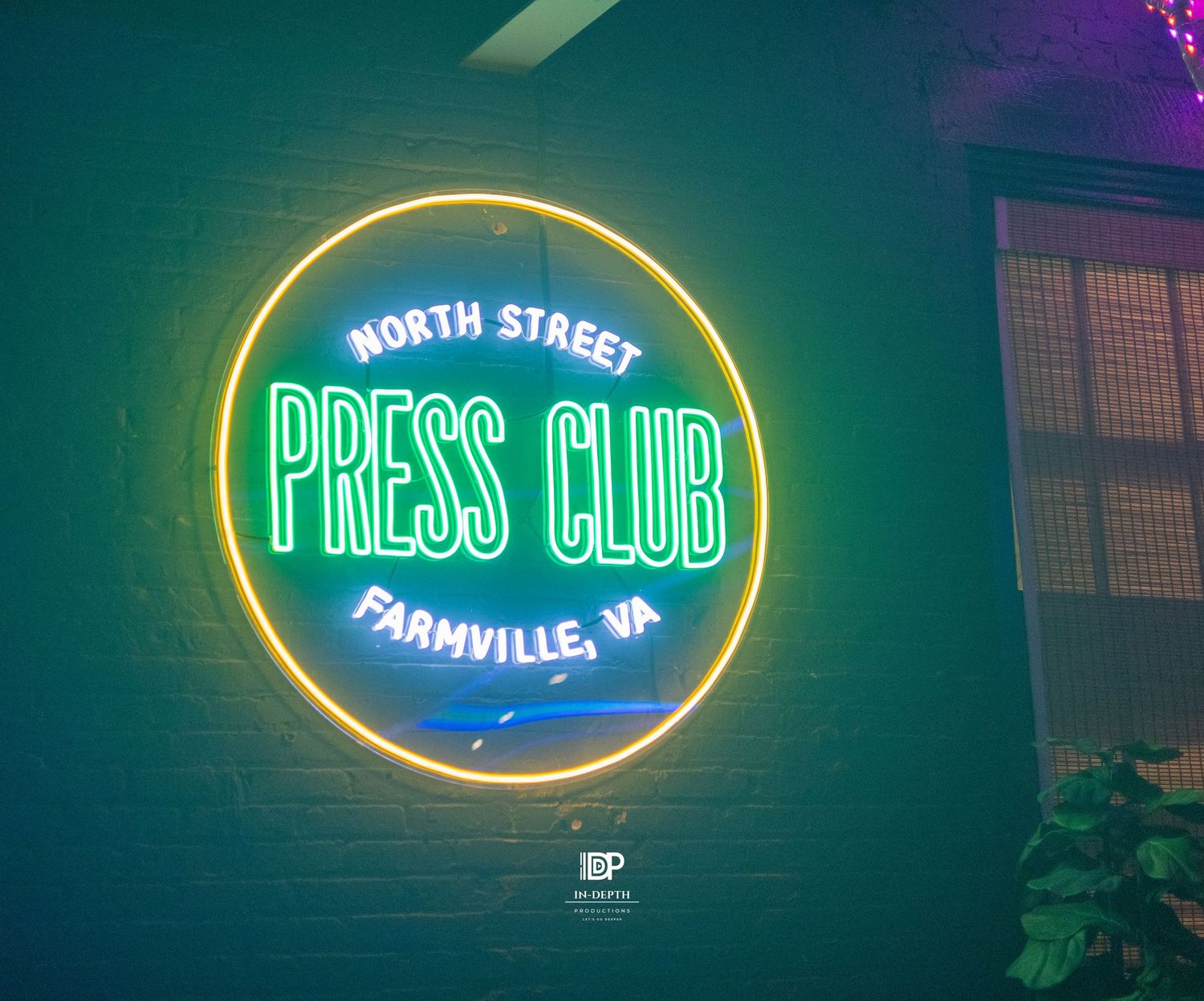 Neon sign for North Street Press Club in Farmville, VA glowing green and yellow on a brick wall.