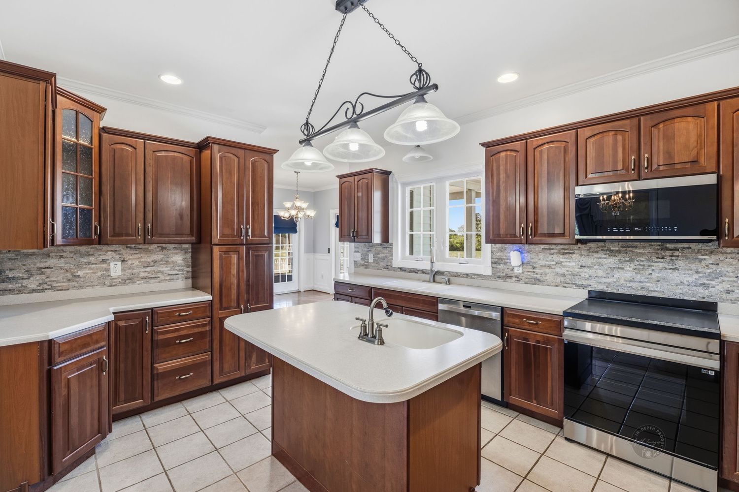 Spacious kitchen with cherry wood cabinets, white countertops, center island, stainless appliances, and tile backsplash.