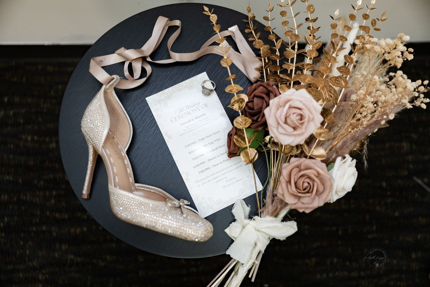 Blush glitter heels, floral bouquet with dried flowers, and elegant wedding invitation on a dark round table.