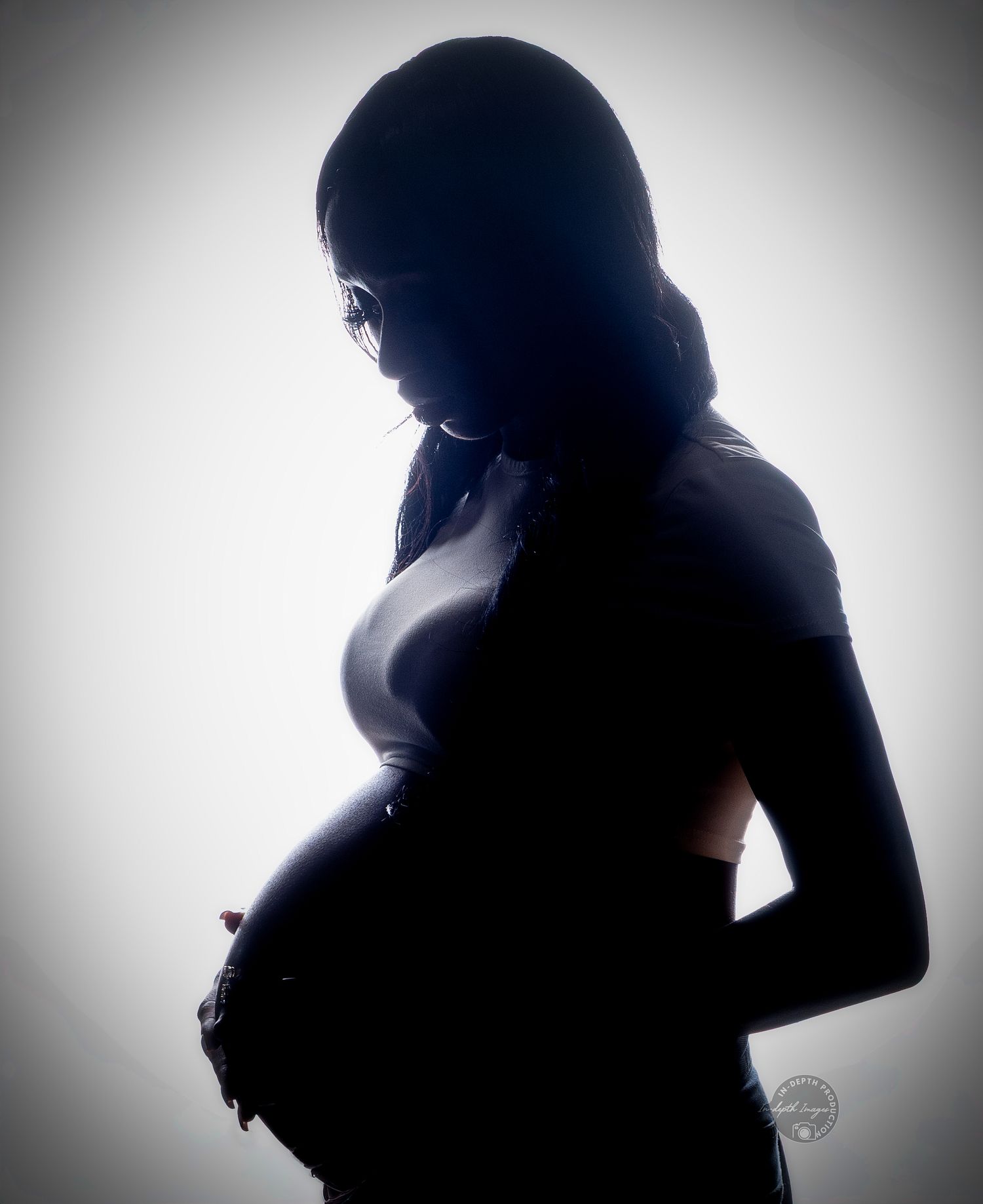Silhouette of a pregnant woman in profile against a bright white background, showcasing her baby bump.