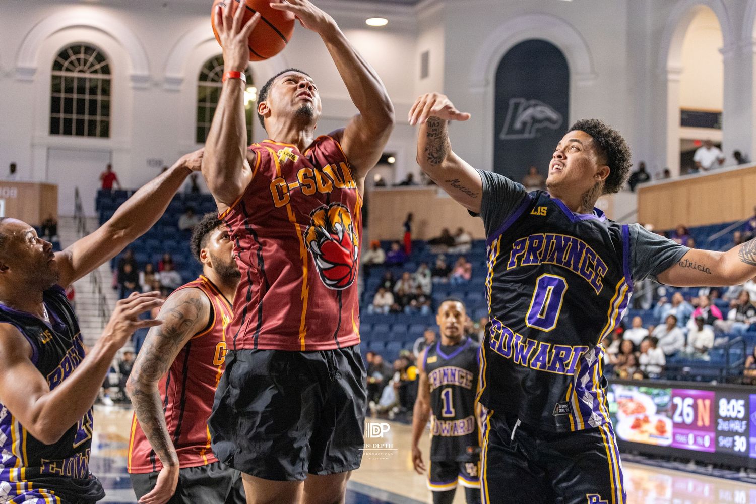 College basketball players compete for a rebound during an intense game, with players in red and purple uniforms.