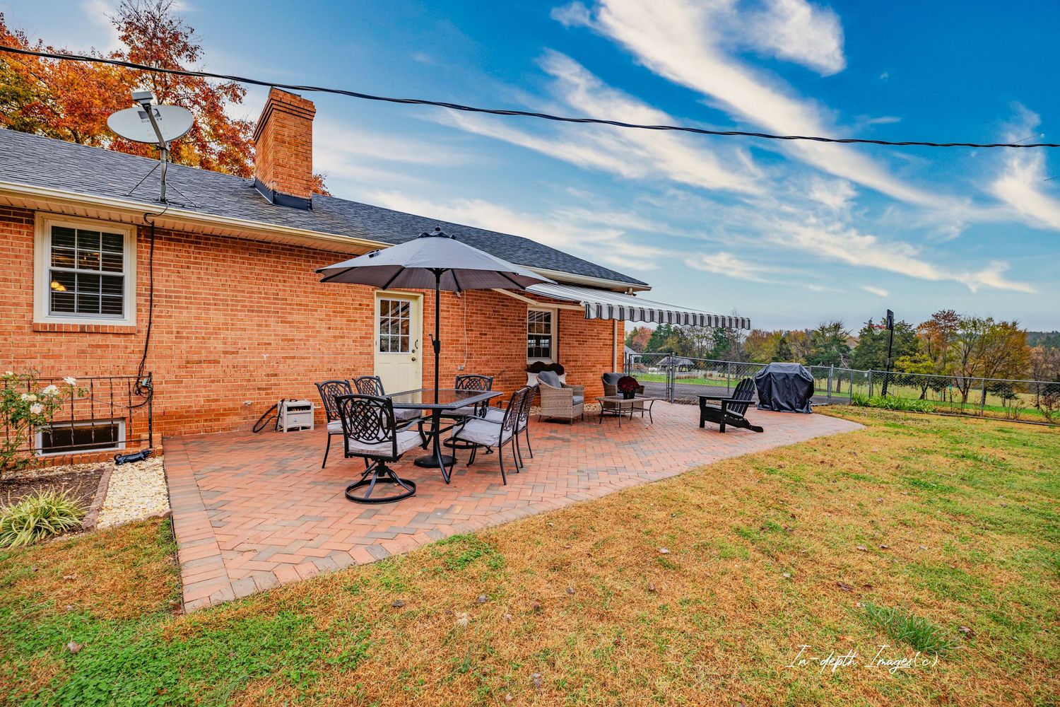 Brick ranch home with a patio featuring outdoor dining set and umbrella overlooking a scenic green landscape.