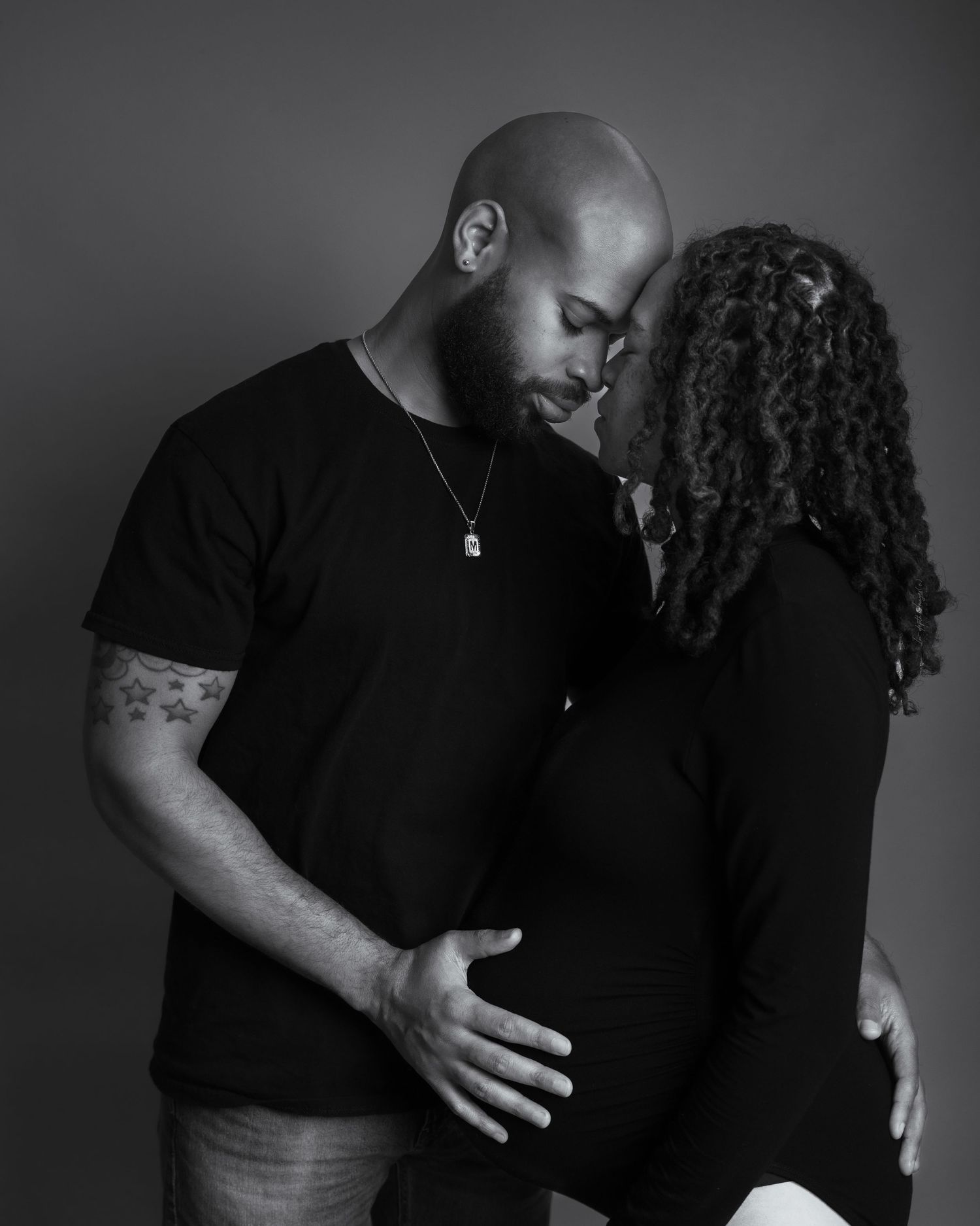 Black and white maternity photo of couple embracing tenderly in studio.