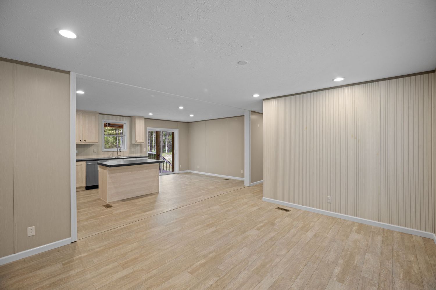 Spacious open-plan living area with light wood floors, recessed lighting, kitchen island, and neutral beige walls.