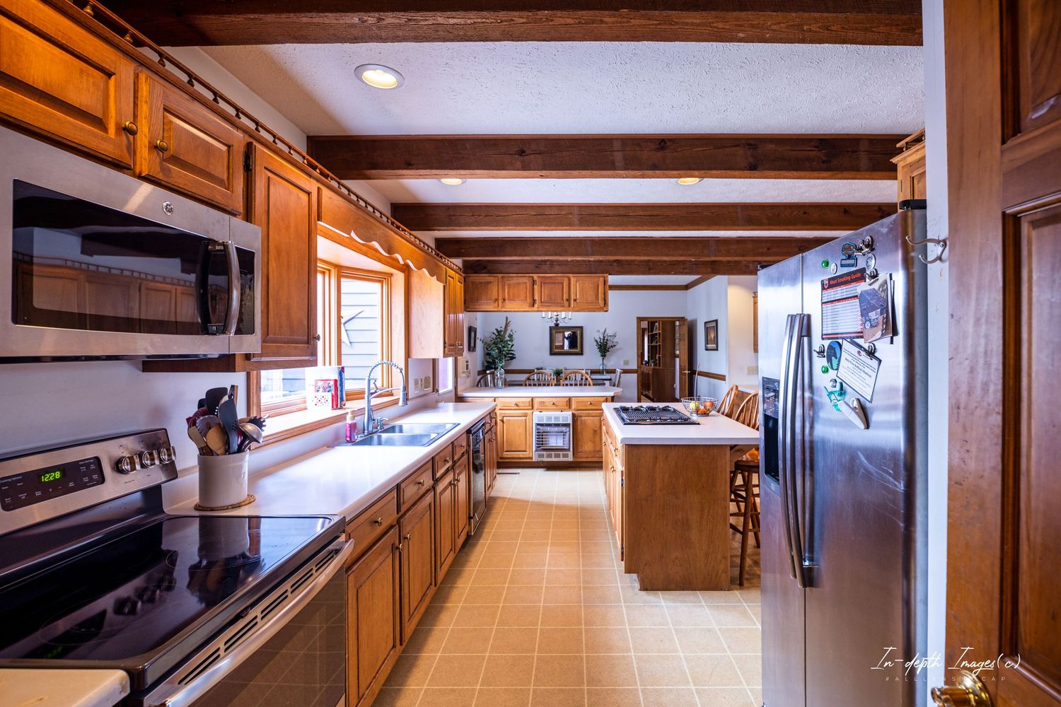 A spacious rustic kitchen featuring wood cabinets, exposed beam ceiling, and stainless steel appliances.