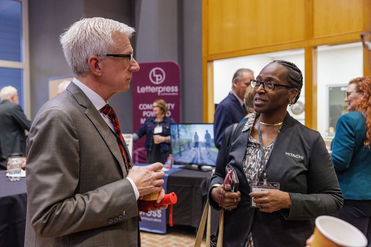 Two professionals networking at a business conference event, engaged in conversation near exhibition booths.