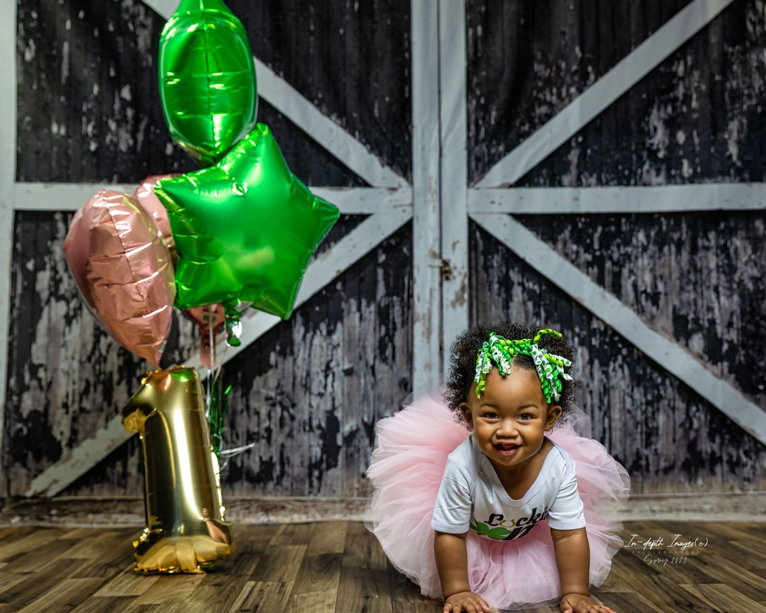 Adorable baby girl in pink tutu crawling beside gold number one balloon at rustic barn birthday shoot.