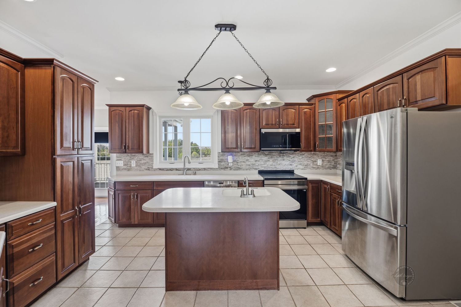Spacious kitchen with dark cherry wood cabinets, stainless steel appliances, center island, and light tile flooring.