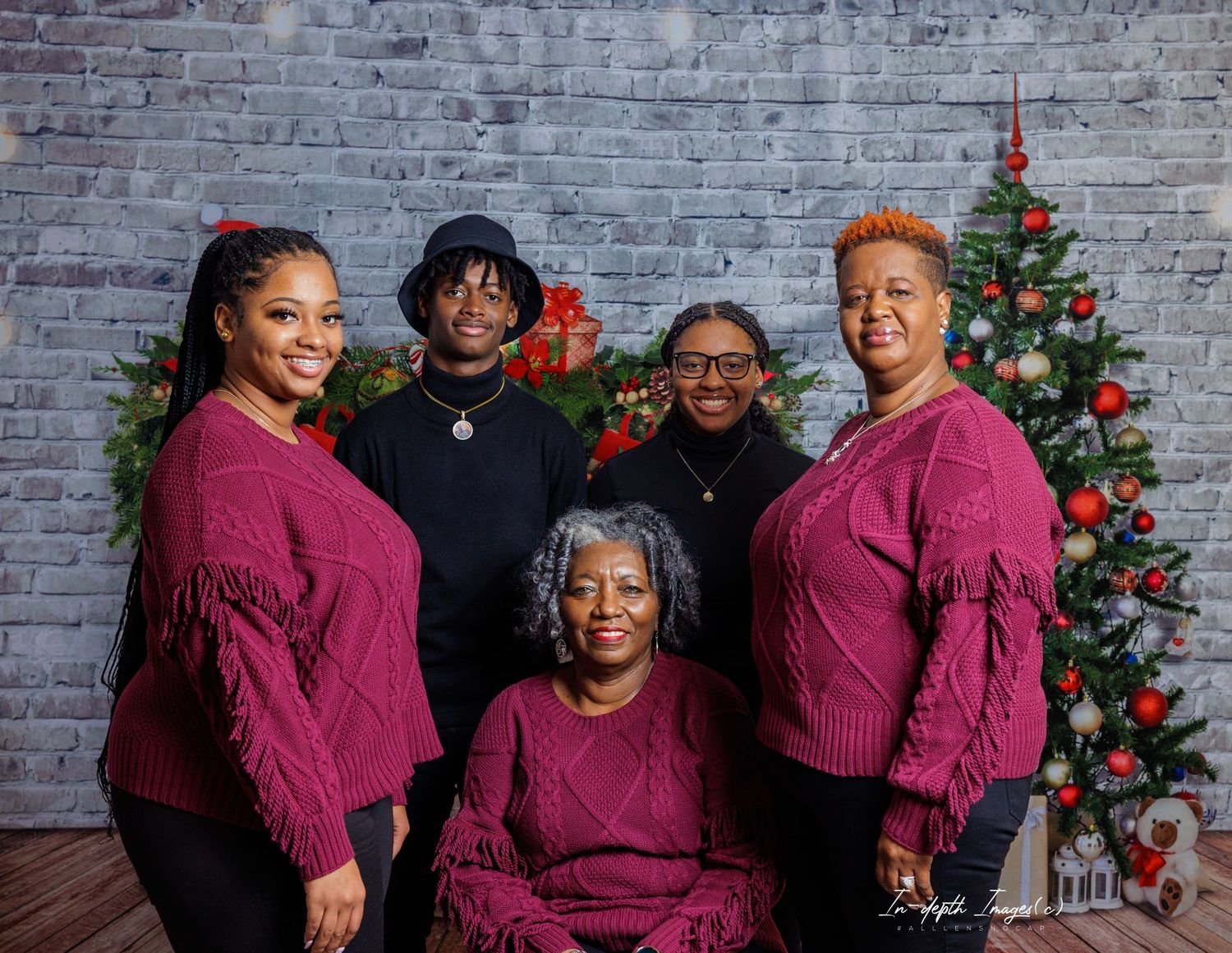 Family of five in matching burgundy sweaters posing by Christmas tree.