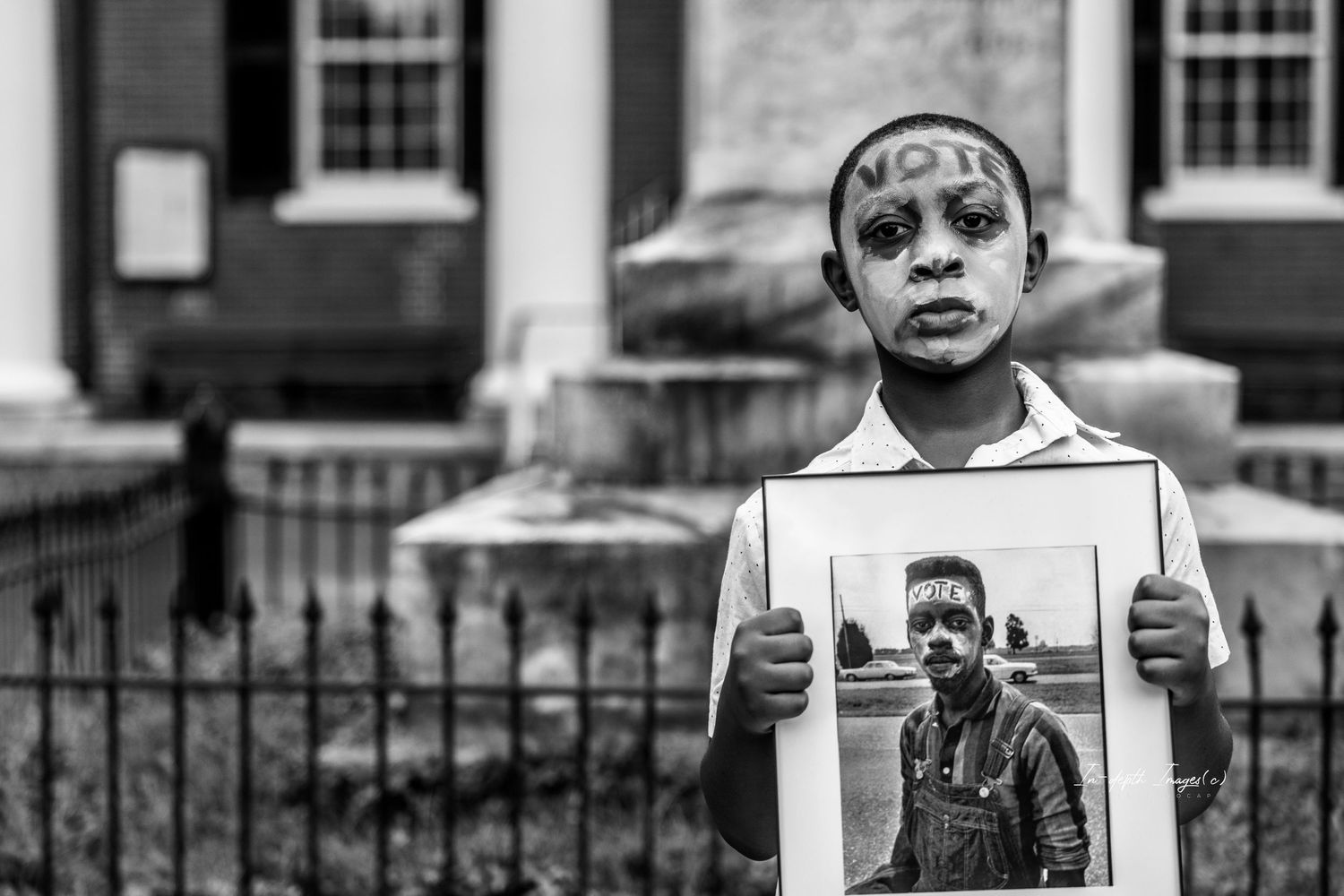 Black and white photo of a child holding a portrait with VOTE written on their forehead.